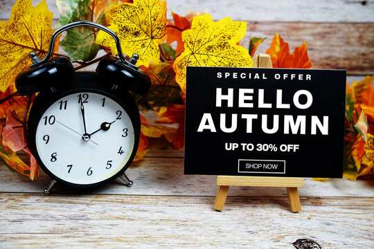 Hello Autumn Sale 30% off Special Offer text with alarm clock and maple leaf decoration on wooden background