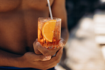 Man holding aperol spritz cocktail with orange slice and ice on beach