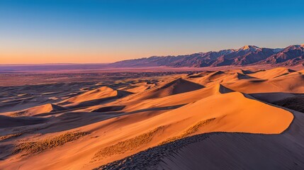 Aerial View of Desert Dunes Under Clear Blue Sky and Mountain Range During Golden Hour