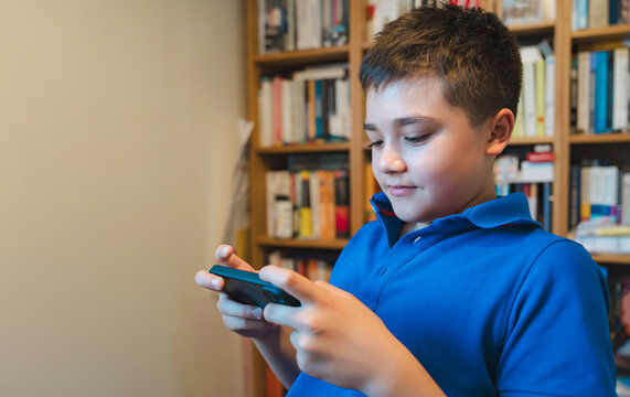 School kid using smartphone research in library with blurry bookshelves.Teen boy using phone study in library,Concept digital technology learning for academic success,AI learning in modern education