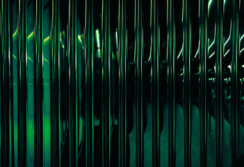 Green tinted glass panels arranged vertically create a lattice or louver effect, illuminated by green light. This type of glass is often used in architecture for its functional and aesthetic benefits.