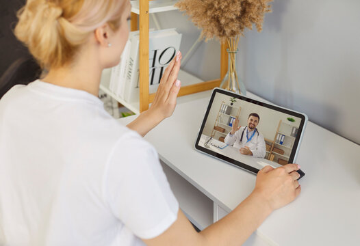 Female sick patient waving hand talking online with young male doctor during video call by virtual webcam using tablet at home. Woman having medical consultation. Telemedicine concept. - Powered by Adobe