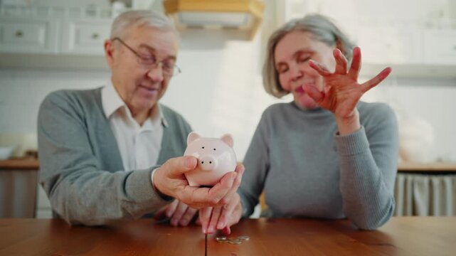 Financial literacy and care about future, old people saving money in piggy bank. Portrait of happy senior spouses in home kitchen interior, economy and family budget, save pocket money, put coins