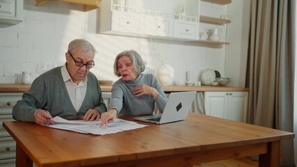 Aged man and his wife controlling utility bills, checking bank papers at home. Grey-haired woman and her husband discussing finance and family budget in kitchen, save money and pay for mortgage