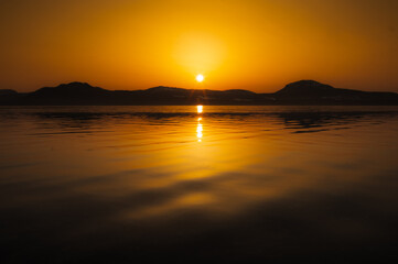 夜明けの湖に朝陽の昇る瞬間。風景は濃いオレンジ色に染まる。