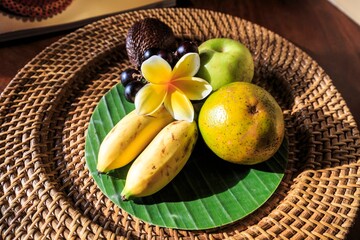 Tropical Fruit Offering with Frangipani on Banana Leaf and Rattan Plate