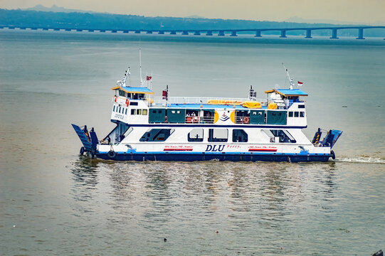 A joko tole ferry ship sails through the water, connecting surabaya and madura. The ferry has a blue and white color scheme and is carrying passengers, indonesia, 14 november 2025.