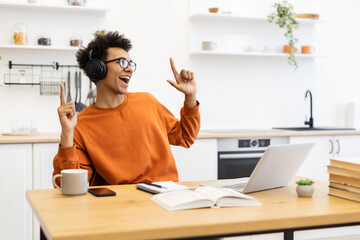 A young man with glasses and headphones is enjoying music while working on a laptop at home.