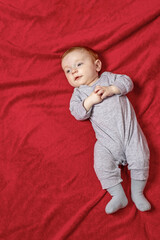 Top view of cute baby boy with an expression of surprise lying on red blanket. Vertically. 