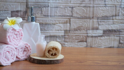 A stack of soft towels with a loofah and a bottle of body wash, representing self-care, on white.Woman using soap dispenser indoors, closeup view