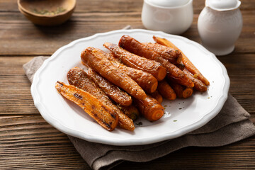 Roasted baby carrots roots with herbs on plate wooden table