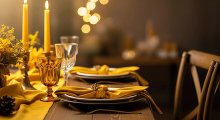 Elegant autumn dinner table setting with yellow linen, burning candles and blurred warm bokeh background.