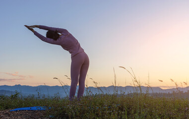 Fitness girl practicing yoga on mountain sunset sky background