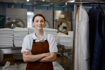 A woman worker in an apron stands with arms crossed in a laundromat