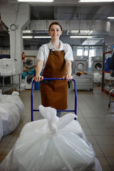 Female worker pushes a cart full of white sheets in a laundromat