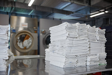 A stack of clean towels is on a table in front of a washing machine