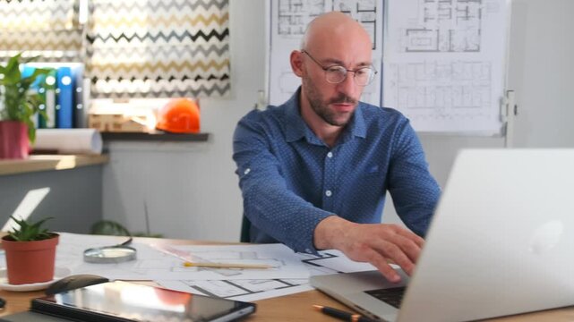 architect examines blueprints carefully, an architect meticulously evaluates technical drawings and design layouts, architect thoroughly reviews detailed blueprints amid studio filled with tools