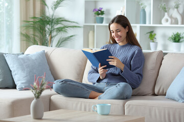 Happy woman in blue reading a paper book at home