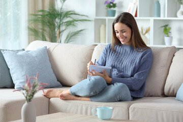 Happy woman in blue writing in a notebook at home