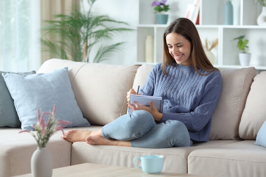 Fototapeta Happy woman in blue writing in a notebook at home