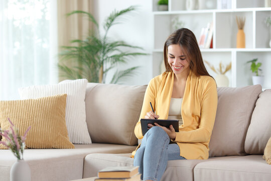 Happy woman in yellow handwriting on digital tablet at home