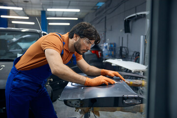 Auto worker sanding car body panel with orange gloves in workshop