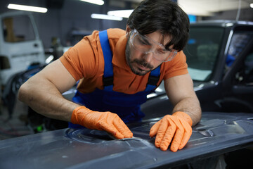 Auto worker sanding car body panel with orange gloves in workshop