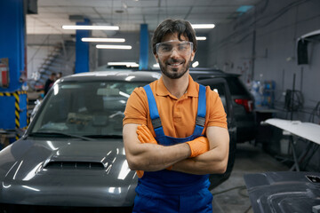 Smiling auto mechanic in garage workshop with car behind