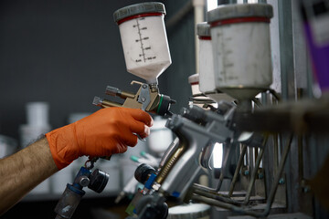 An industrial paint spray gun being used by a technician wearing protective gloves inside a workshop