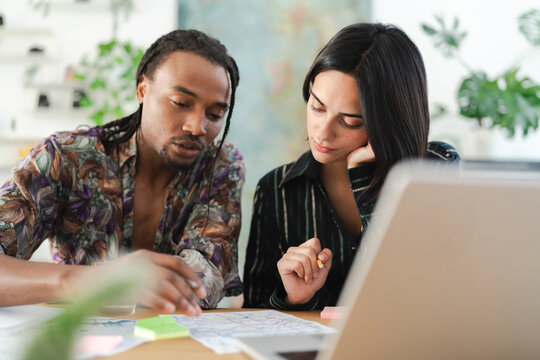 A diverse man and woman collaborate at a desk, reviewing documents and a laptop. They are engaged in a focused discussion, working together on a shared project.