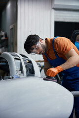 Auto body technician sanding car hood in workshop