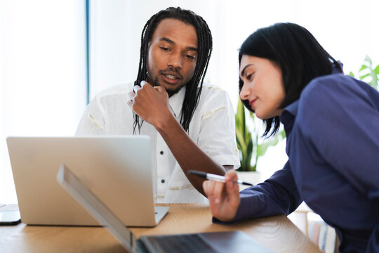 Diverse colleagues collaborate on a project, reviewing information on a laptop. The woman points with a pen while the man listens thoughtfully. They are focused on their work.