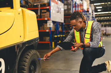 Warehouse worker wearing a safety vest checking a forklift tire with a clipboard and paper,...