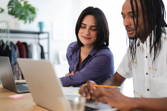 A diverse team of two professionals collaborates on a project, reviewing content on a laptop. They are engaged in a focused discussion at their modern office desk.
