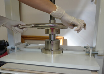 Gloved hands rotate the handle of the screw press. Paper pressing and straightening, bookbinding workshop, close-up.