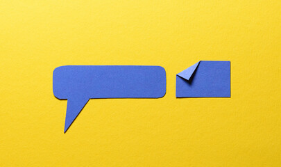 Blue speech bubble and paper memo note with folded dog-ear earmark and copy space for text on yellow background, communication dialog concept top view flat lay