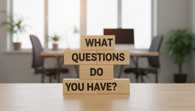 Wooden blocks spelling WHAT QUESTIONS DO YOU HAVE? on a desk in a modern office, representing inquiry, feedback, and open communication.