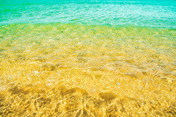 A background of clear water over a sandy bottom. Shallow water with yellow sand. Gentle ripples on the surface. Glittering reflections on the sea.