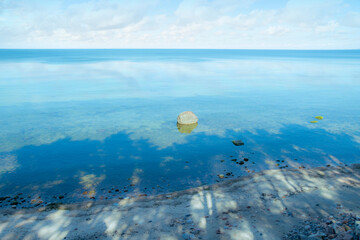 Tree shadows on a high bank. The seashore with sand and calm water.