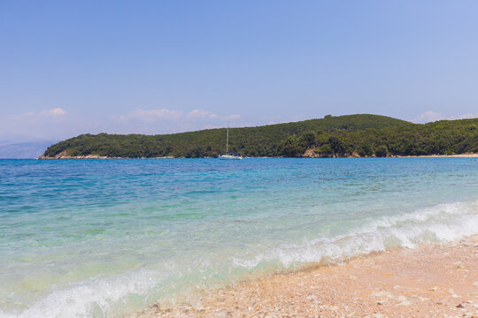 Crystal clear turquoise waters meet golden sandy beach with lush green hills .