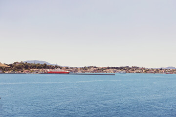 Fototapeta premium Corfu sunlit shoreline and deep blue sea frame docked ships and distant buildings, Greece