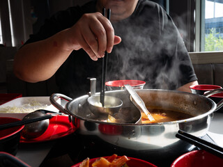Person eating hot pot shabu shabu with chopsticks and steaming broth in divided metal pot at restaurant table