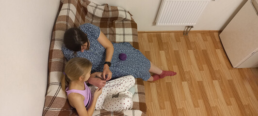 A mother and daughter knit together on the sofa at home.