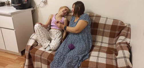A mother teaches her daughter how to knit in the comfort of her home kitchen, and they laugh.