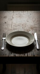 Empty white dish with a fork and knife on a rustic dark wooden table. Concept of poverty, hunger, diet, or a finished meal.