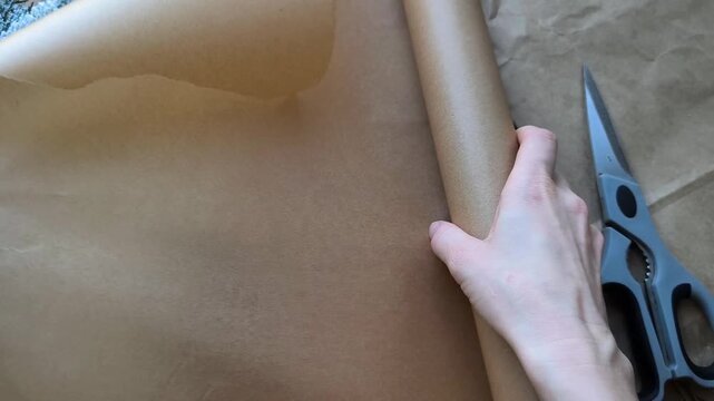 woman's hand unrolls a roll of kraft paper. Eco-friendly gift wrapping materials. Christmas recycling sign.