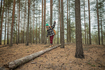Cheerful woman carefully walking along fallen pine trunk, maintaining balance with backpack. Female hiker adventure in autumnal fall woodland, enjoying outdoor challenge, solo forest trekking