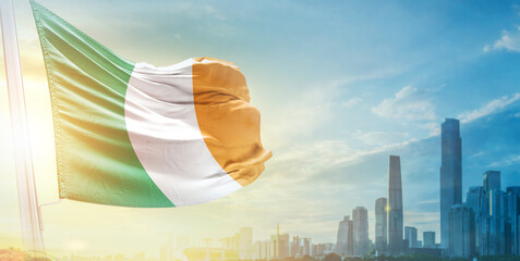 Ireland flag wavering in beautiful clouds with building skyline. The flag with drone shot in beautiful sky. Ireland national flag for independence day.