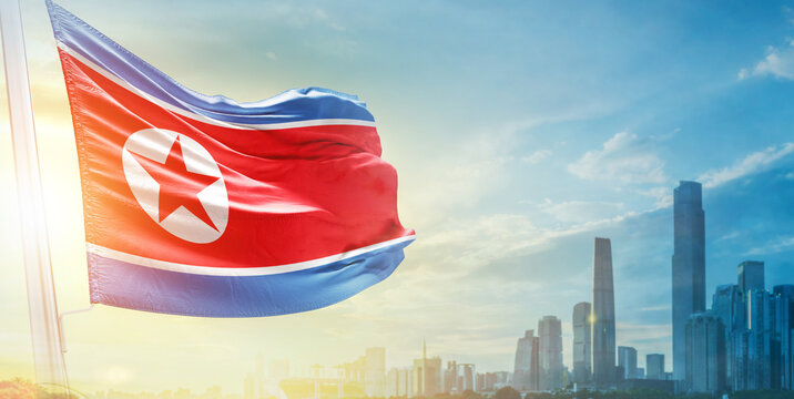 North Korea flag wavering in beautiful clouds with building skyline. The flag with drone shot in beautiful sky. Korea national flag for independence day. - Powered by Adobe