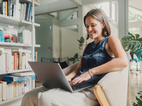 Smiling woman studying with laptop in modern home living room